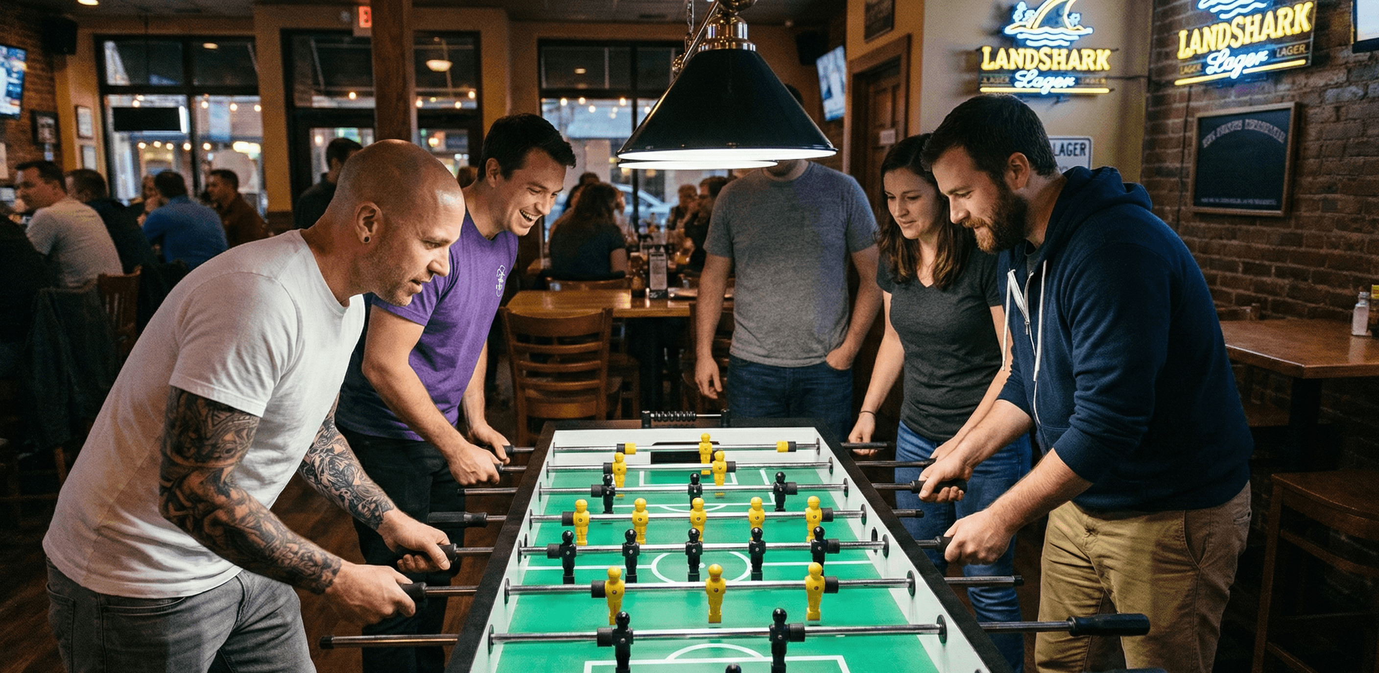 A group of four plays foosball in a bar.