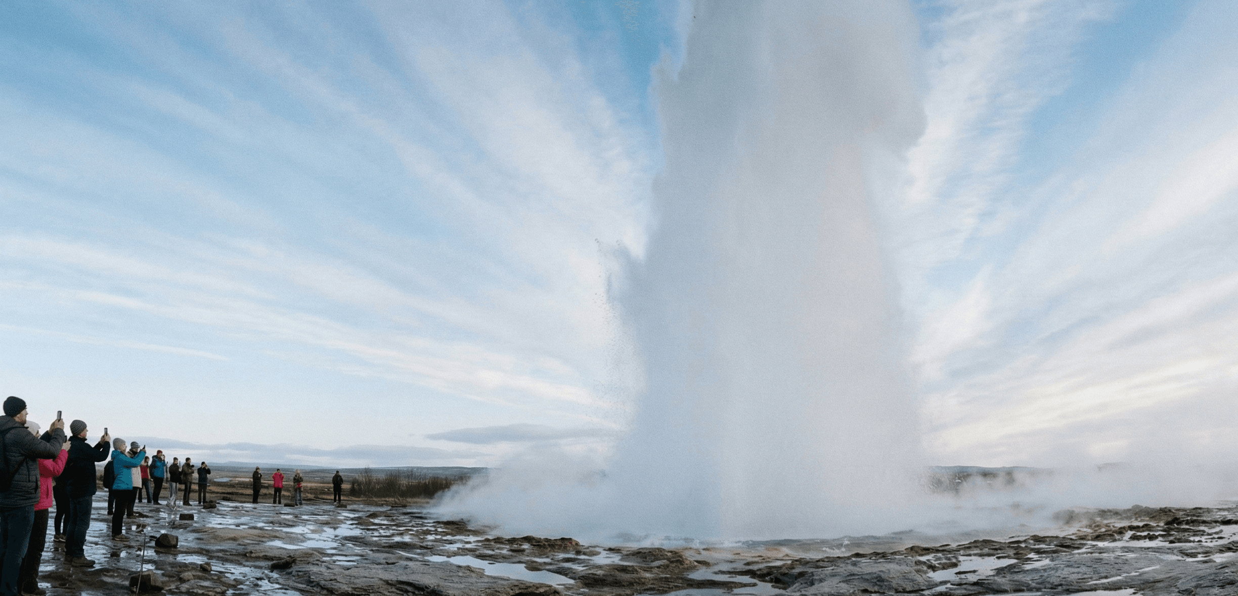 A geyser erupts in front of tourists.