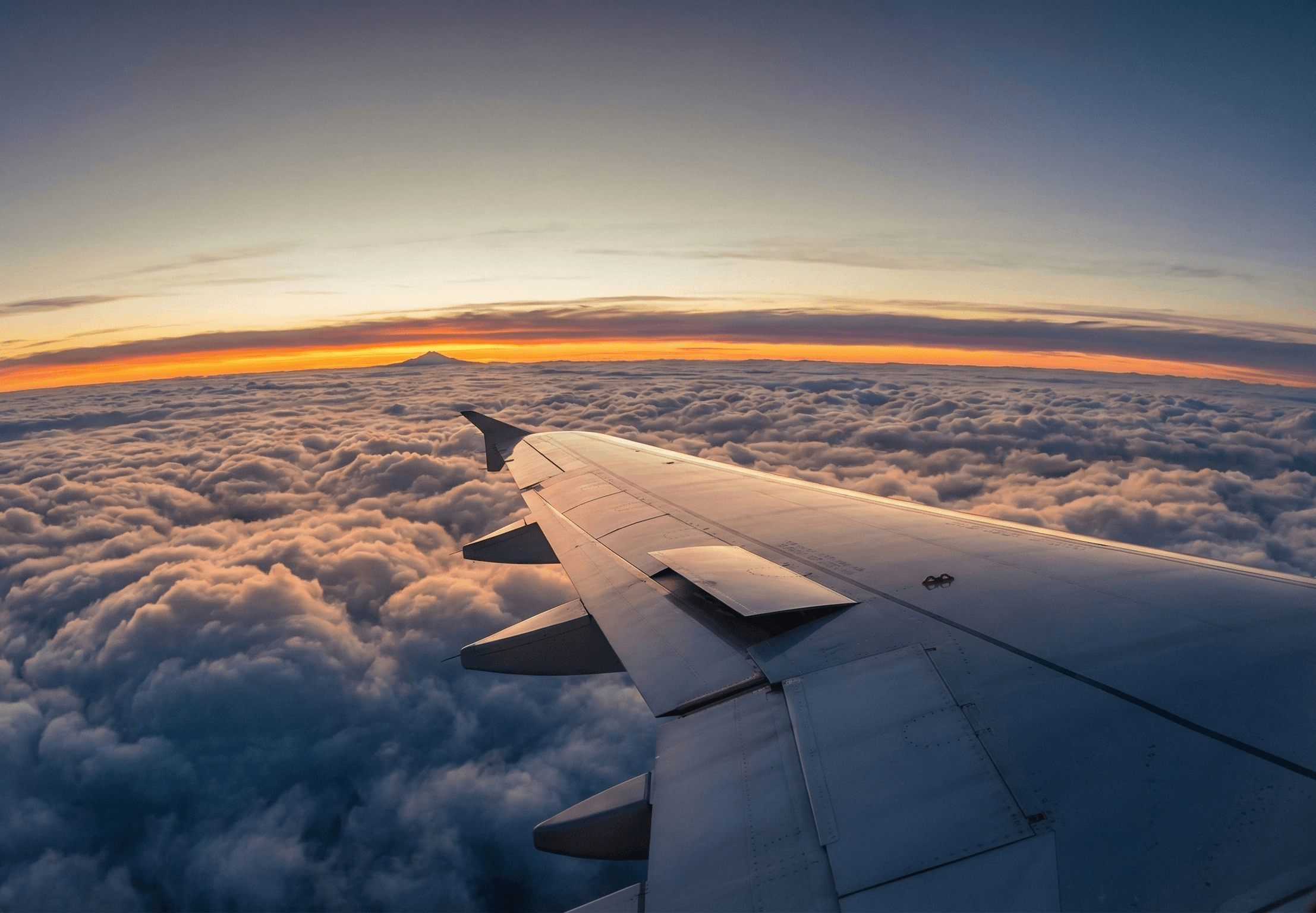 A wing of an airplane over a canopy of clouds at sunset.